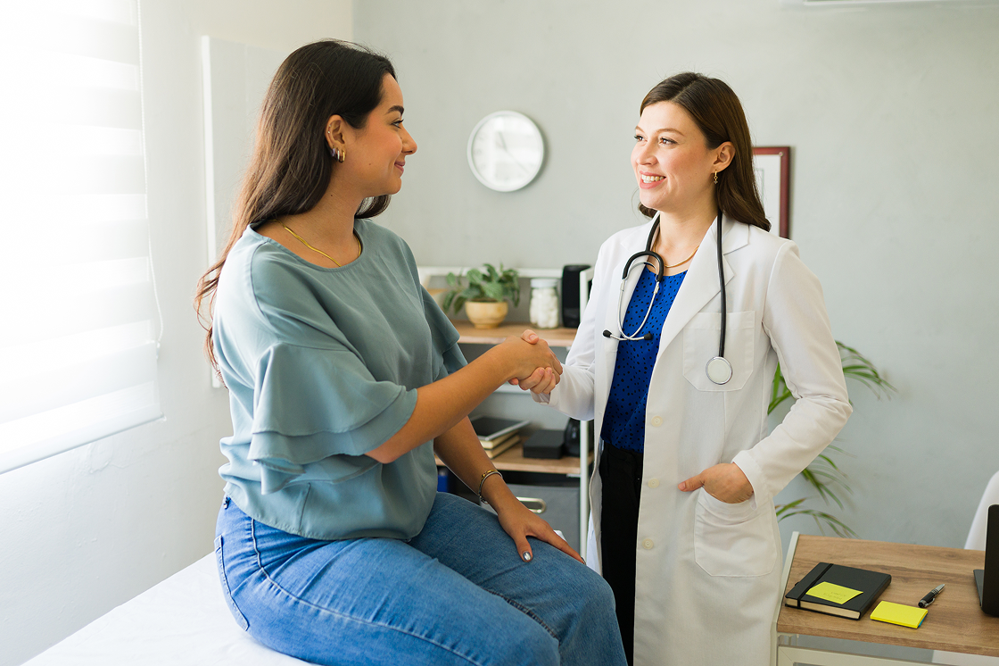 Ärztin begrüßt Patientin im Sprechzimmer mit Handschlag  