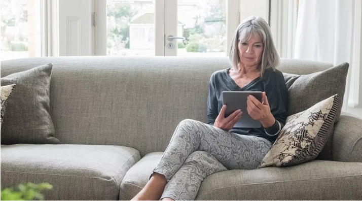 Ältere Frau sitzt auf dem Sofa und liest auf einem Tablet